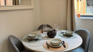 Ruokailutilassa on pyöreä pöytä, johon on katettu neljälle, tuolit, ikkuna, josta avautuu näkymä rakennuksiin, sekä kaksi kehystettyä kaupunkimaisemapiirrosta seinällä.