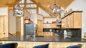 A modern kitchen with wooden cabinets, a large island with bar stools, and pendant lighting. - Mountain Memories-Luxury Lodge w/Views, Hot Tub (Maggie Valley)