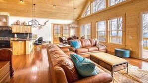 A spacious living area with a wooden ceiling, large windows, a kitchen, and a cozy seating arrangement. - Mountain Memories-Luxury Lodge w/Views, Hot Tub (Maggie Valley)