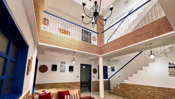 A spacious living area with a brown sofa, a staircase, and a chandelier. - auberge dar fayçal (Mirleft)