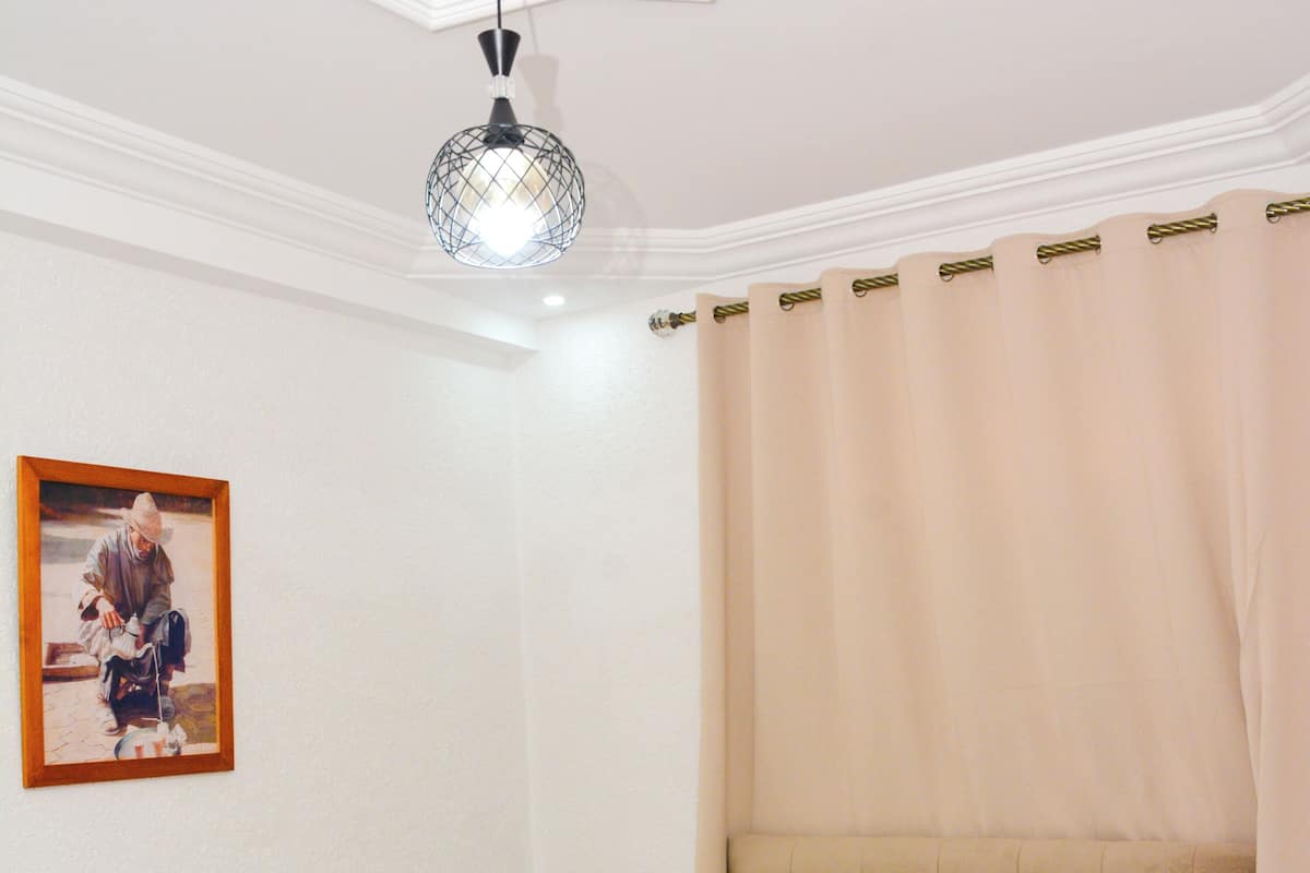 A bedroom with a bed, a headboard, a bedside table, a lamp, and a framed picture on the wall.