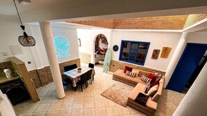 A spacious living area with a dining table, sofa, and a surfboard. - auberge dar fayçal (Mirleft)
