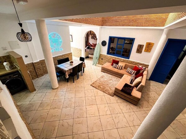 A spacious living area with a dining table, sofa, and a surfboard. - auberge dar fayçal (Mirleft)