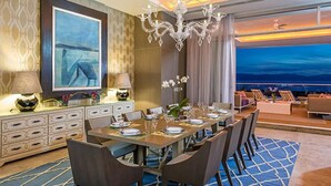 A dining area with a long table set for a meal, a chandelier, and a view of the ocean. - GRAND LUXXE - THE RESIDENCE FOUR BEDROOM TOWER (Las Jarretaderas)