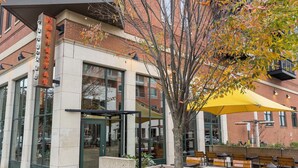 A modern building with a glass entrance, outdoor seating, and a tree with autumn leaves. - Stylish 3BR Retreat Near OSU - Sauna & Fire pit (Columbus)