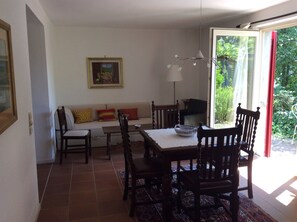 Ein Essbereich mit Tisch, Stühlen, einer Couch und einem Fenster mit Blick ins Grüne.
