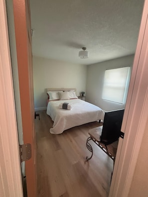 A bedroom with a bed, a bedside table, a chair, and a window with blinds.
