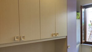 Een kleine kamer met een enkel bed, een kleurrijk quilt, lichte kasten en een raam met uitzicht.
