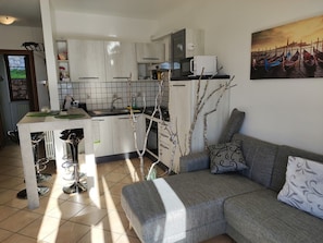A modern kitchen with white cabinets, a tiled backsplash, and a dining area with bar stools. There is a gray sofa with patterned cushions in the living area. - Appartamento Panoramico by Theater Home - with big terrace and marvellous lake view (Tignale)