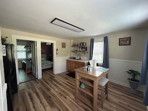 Un espacio habitable compacto con kitchenette, comedor pequeño y un dormitorio.