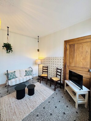 Un salon comprenant un canapĂ©, deux fauteuils, une table basse, un meuble pour la tĂ©lĂ©vision, une plante suspendue et un mur ornĂ© dâun motif.