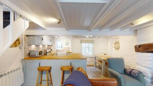 A cozy kitchen with a central island, wooden stools, a blue armchair, and a rustic wooden beam.