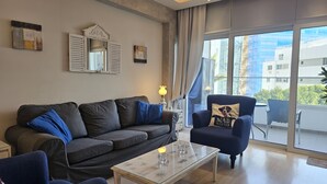 A modern living room with a grey sofa, a blue armchair, and a glass coffee table. - 116 NIC 302b - Stay Armonia Central Suite (Nicosia)