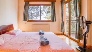 Un dormitorio con cama, un radiador, una ventana con cortinas y un ventilador de pie.