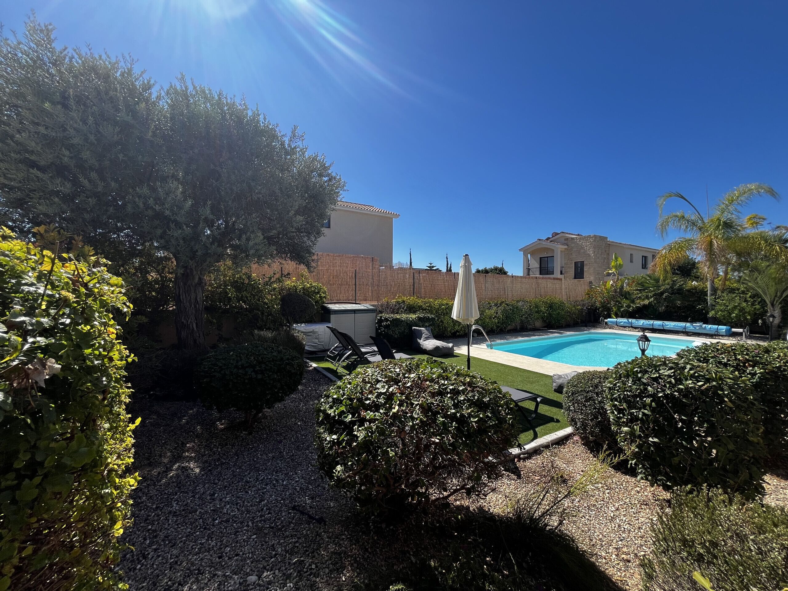 A backyard with a swimming pool, a covered barbecue area, and a stone wall.