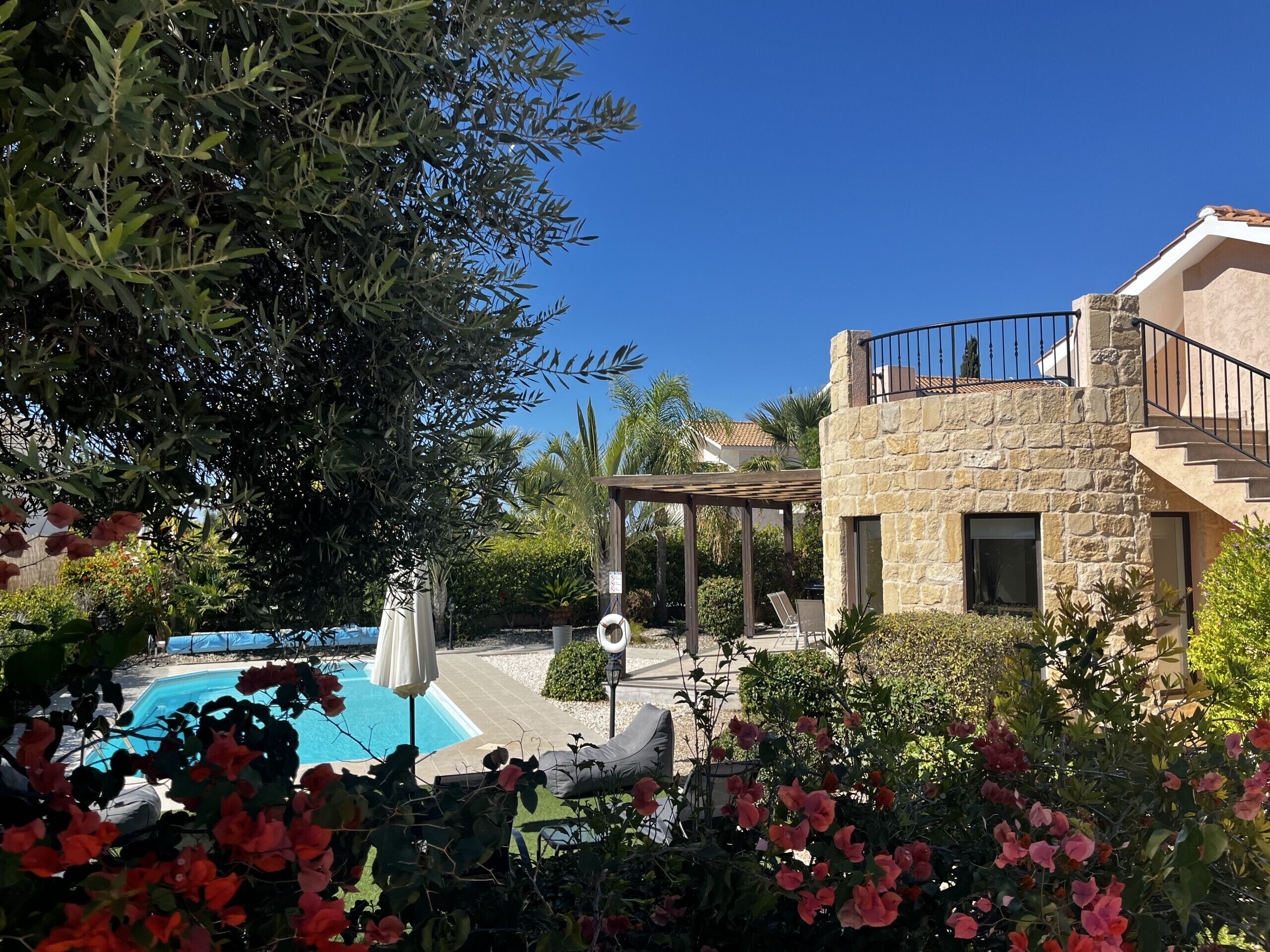 Zona de piscina amb edifici de pedra, una pèrgola i vegetació abundant.