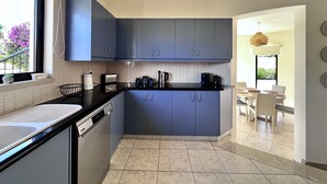 Una cocina moderna con armarios grises, encimera negra y lavavajillas. Se ve una ventana con vistas a flores púrpuras.