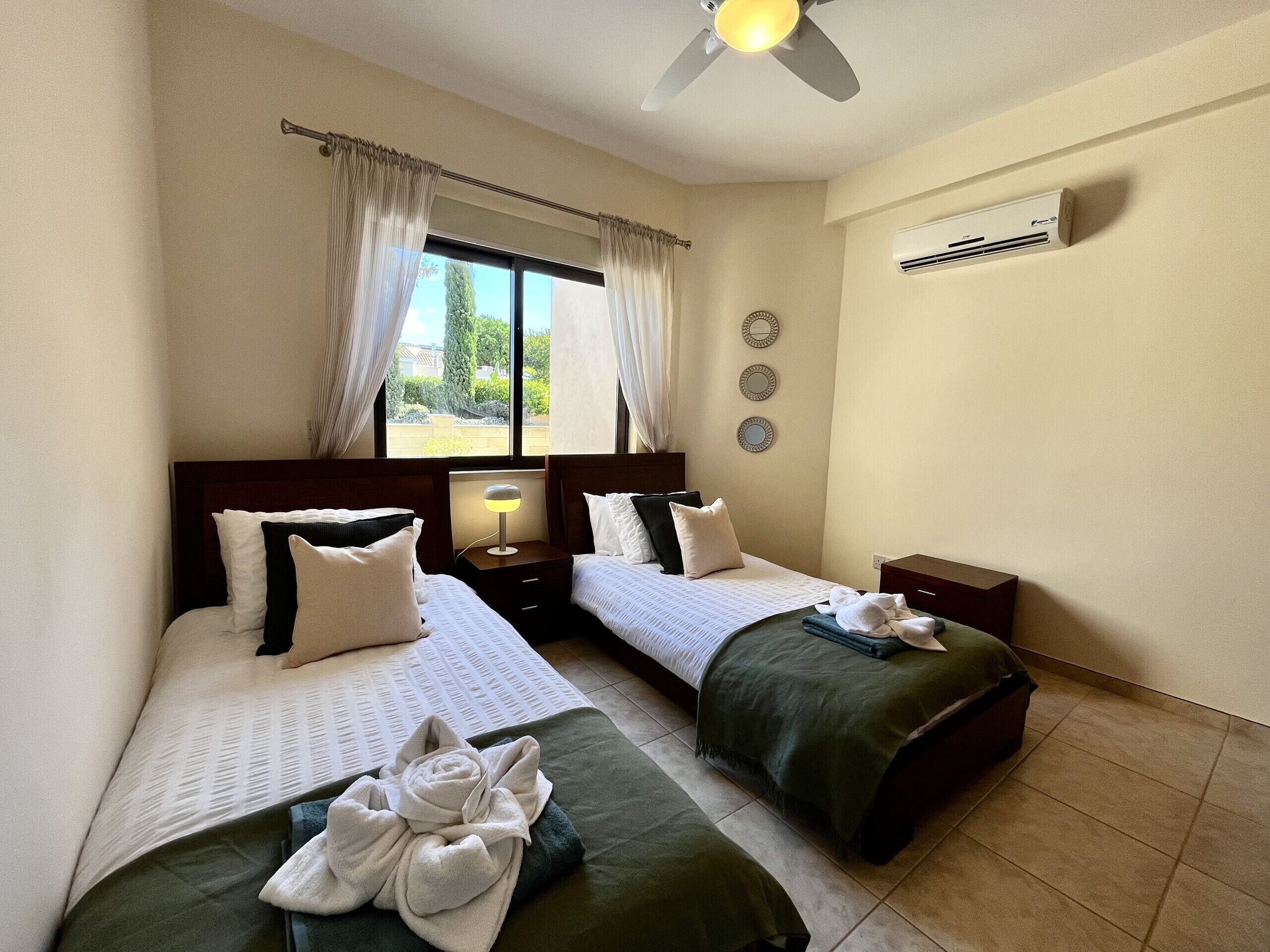Une chambre d’hôtel avec deux lits, un ventilateur de plafond, un appareil de climatisation et une fenêtre avec des rideaux.
