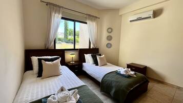 Une chambre d’hôtel avec deux lits, un ventilateur de plafond, un appareil de climatisation et une fenêtre avec des rideaux.