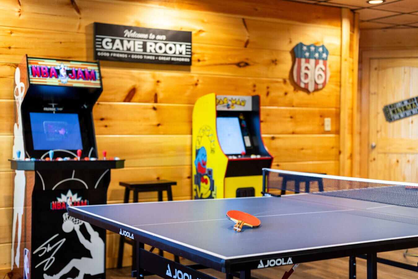 Et spil rum med en NBA JAM arkademaskine, et bordtennisbord og et velkomstskilt.
