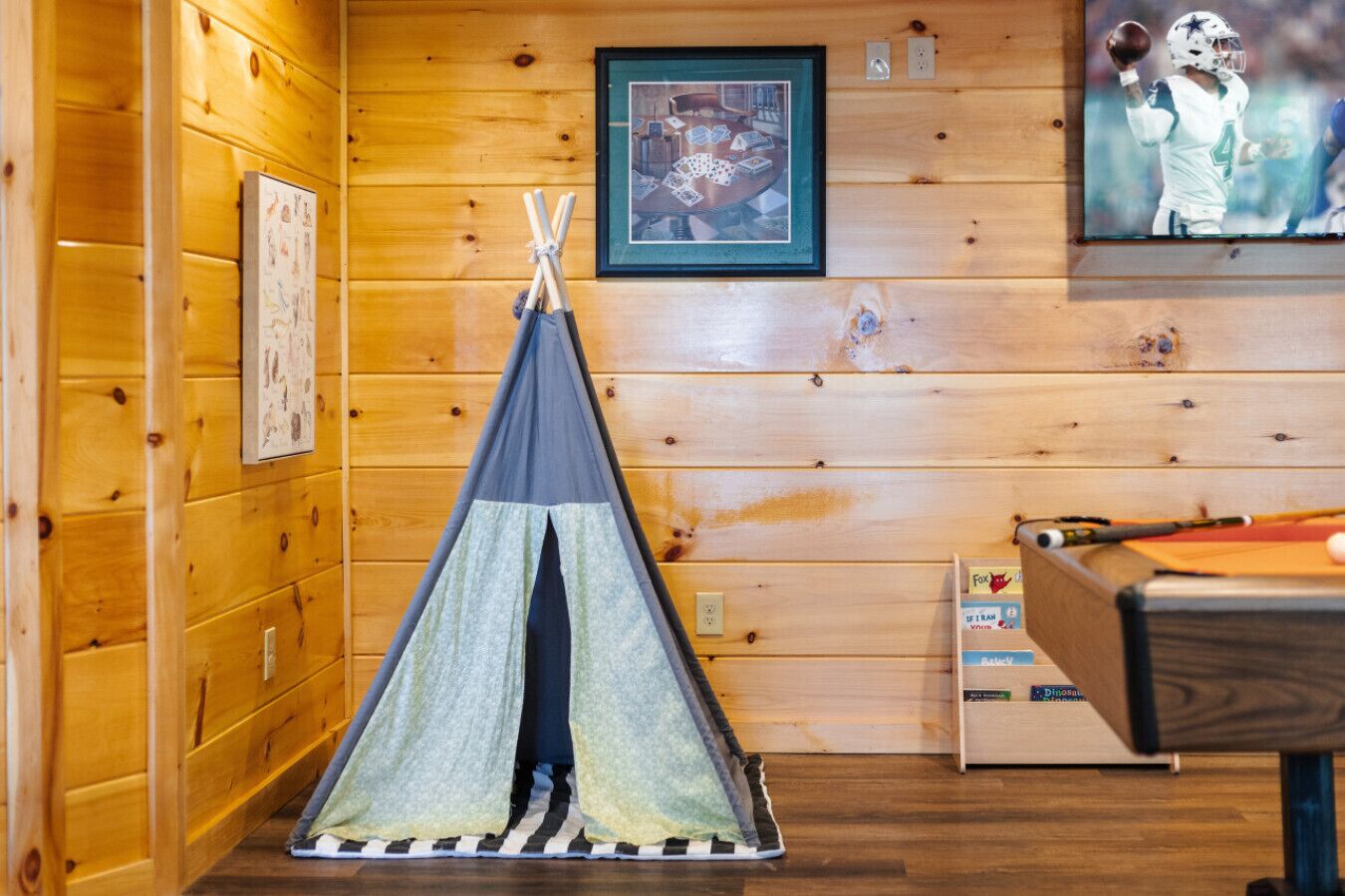 A cozy room with wooden walls, a framed picture, a teepee, and a pool table.