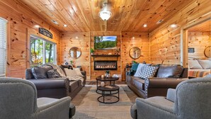A cozy cabin interior with wooden walls, a fireplace, leather sofas, and a round coffee table. - Twin Summit Resort (Sevierville)