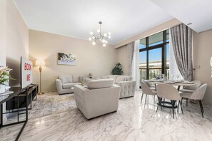 A modern living room with a sofa, armchairs, a dining table with chairs, a floor lamp, and a large window with curtains. - StayShort - Hidden Jewel 1 minute walk from Al Furjan Metro Sleeps 5 (Dubai)