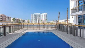 Ein rechteckiger Swimmingpool mit blau gefliestem Becken, umgeben von einem Metallzaun und Palmen.