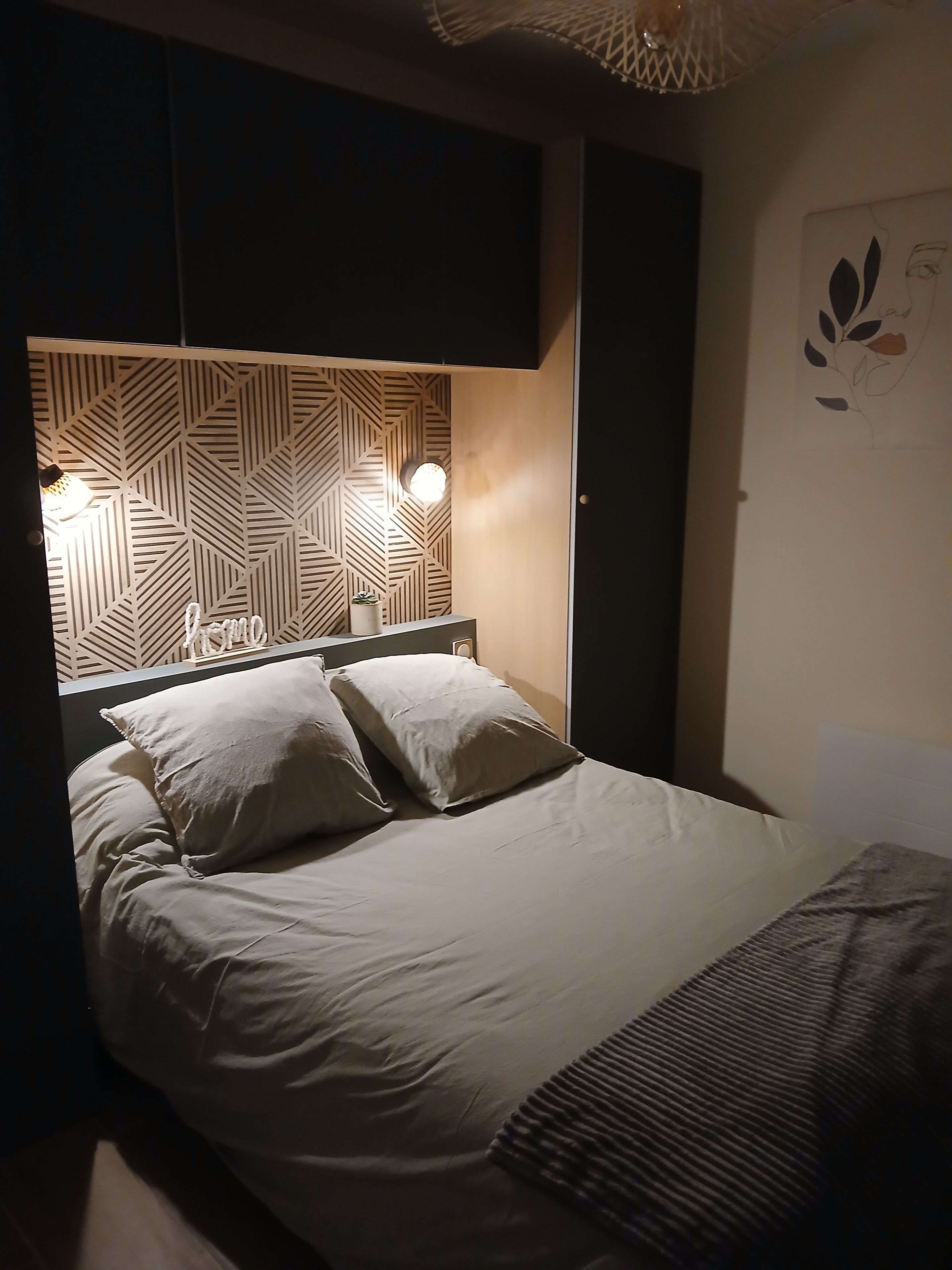 Ein ordentlich bezogenes Bett mit einem Kopfstück im geometrischen Muster, einer Nachttischlampe und einem Wandbild.