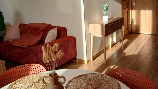 Una sala de estar con un sofá rojo, una mesa de centro con individuales tejidos y un jarrón con flores secas.
