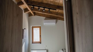 Ein schmaler Gang mit Holzbalken an der Decke, einem Fenster mit Steinwand und einem weißen Heizkörper.