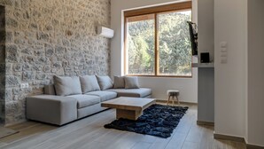 Ein modernes Wohnzimmer mit Steinwand, großem Fenster, beigefarbenem Sofa, Couchtisch aus Holz und schwarzem Teppich.