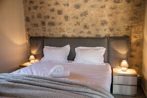 Un lit bien fait, avec du linge de lit blanc, deux oreillers et une serviette pliée posée sur le côté. Deux lampes de chevet sont placées sur des tables de chevet en bois.