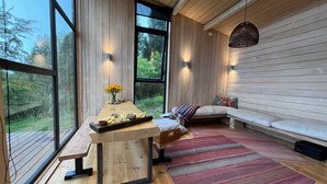 A modern interior with a wooden dining table, bench seating, and a large window offering a view of greenery. - Ampe Lodge (Puerto Varas)