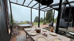A covered outdoor dining area with a table set for four, a hot tub, and a grill. - Ampe Lodge (Puerto Varas)