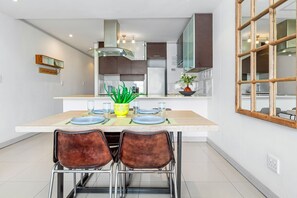 A modern kitchen with a central island, stainless steel appliances, and a dining area with two chairs. - The Quadrant 406 (Cape Town)
