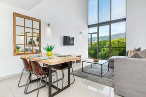 A modern interior with a dining area, a sofa, and a large window offering a view of greenery and mountains. - The Quadrant 406 (Cape Town)