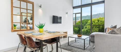 A modern kitchen with a dining area, large windows, and a view of greenery.
