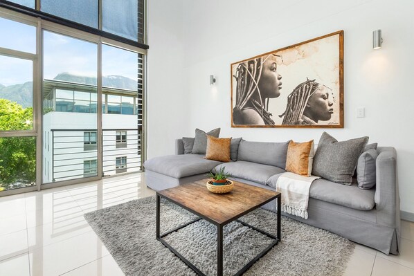 A modern living room with a grey sofa, a wooden coffee table, and a large framed artwork on the wall. - The Quadrant 406 (Cape Town)