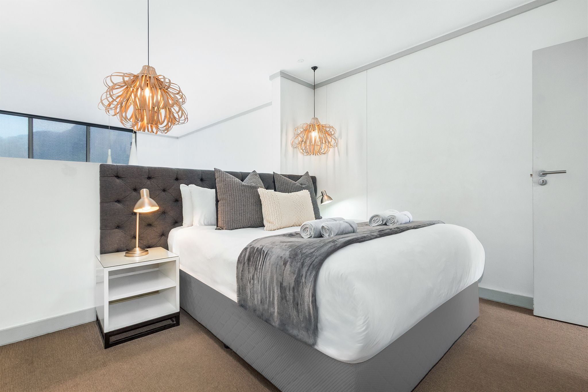 Ein modernes Schlafzimmer mit einem großen Bett, zwei Pendelleuchten, einem Nachttisch und Blick ins Freie.