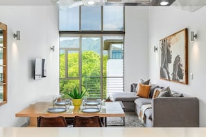 A modern dining area with a wooden table set for four, a sofa with cushions, and a large window offering a view of greenery and mountains. - The Quadrant 406 (Cape Town)