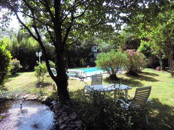 Un patio trasero con piscina, un pequeño pabellón y una mesa con sillas.