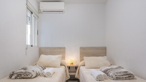 Une petite chambre propre, équipée de deux lits, d’une table de chevet, d’une lampe et d’un appareil de climatisation.
