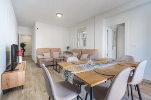 Moderni olohuone, jossa on ruokailutila, sohvaryhmä, televisio ja puinen kaappi.
