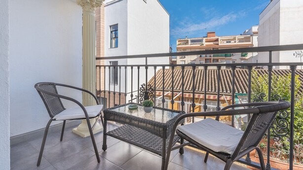Un balcon avec deux fauteuils en osier, une table en verre et une plante en pot.