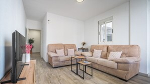 Un salon équipé d’un téléviseur à écran plat, d’un canapé beige, d’une table basse en bois et d’une petite table d’appoint sur laquelle est posée une plante.