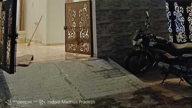A modern building with a glass facade, a decorative entrance gate, and a parked motorcycle. - HOTEL MANGALAM REGENCY (Indore)