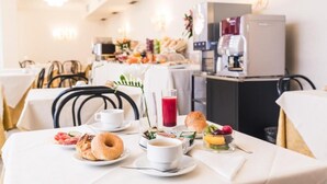 Une table mise pour le petit-déjeuner, avec une place pour deux personnes, comprenant un croissant, du café, du jus de fruits et un panier de fruits.