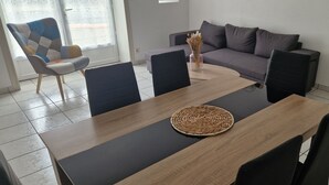 A dining area with a wooden table, black chairs, a woven placemat, and a grey sofa. - Gîte near Puy du Fou (Montournais)