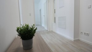 A hallway with a potted plant, light wooden flooring, white walls, and a door at the end.